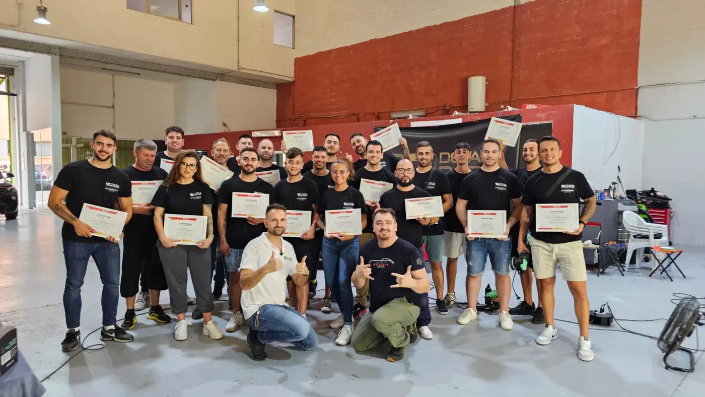 Decenas de alumnos de Academia Detail posando con sus diplomas en la nave