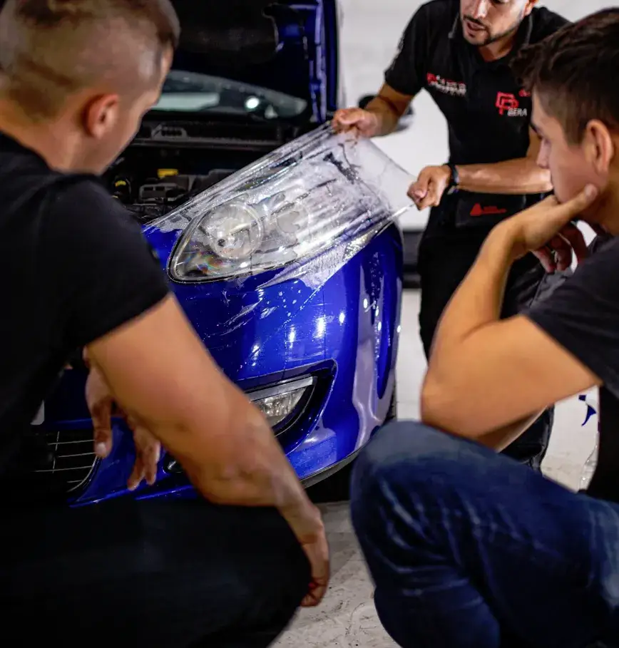 Alumnos aprendiendo a instalar PPF en un coche azul