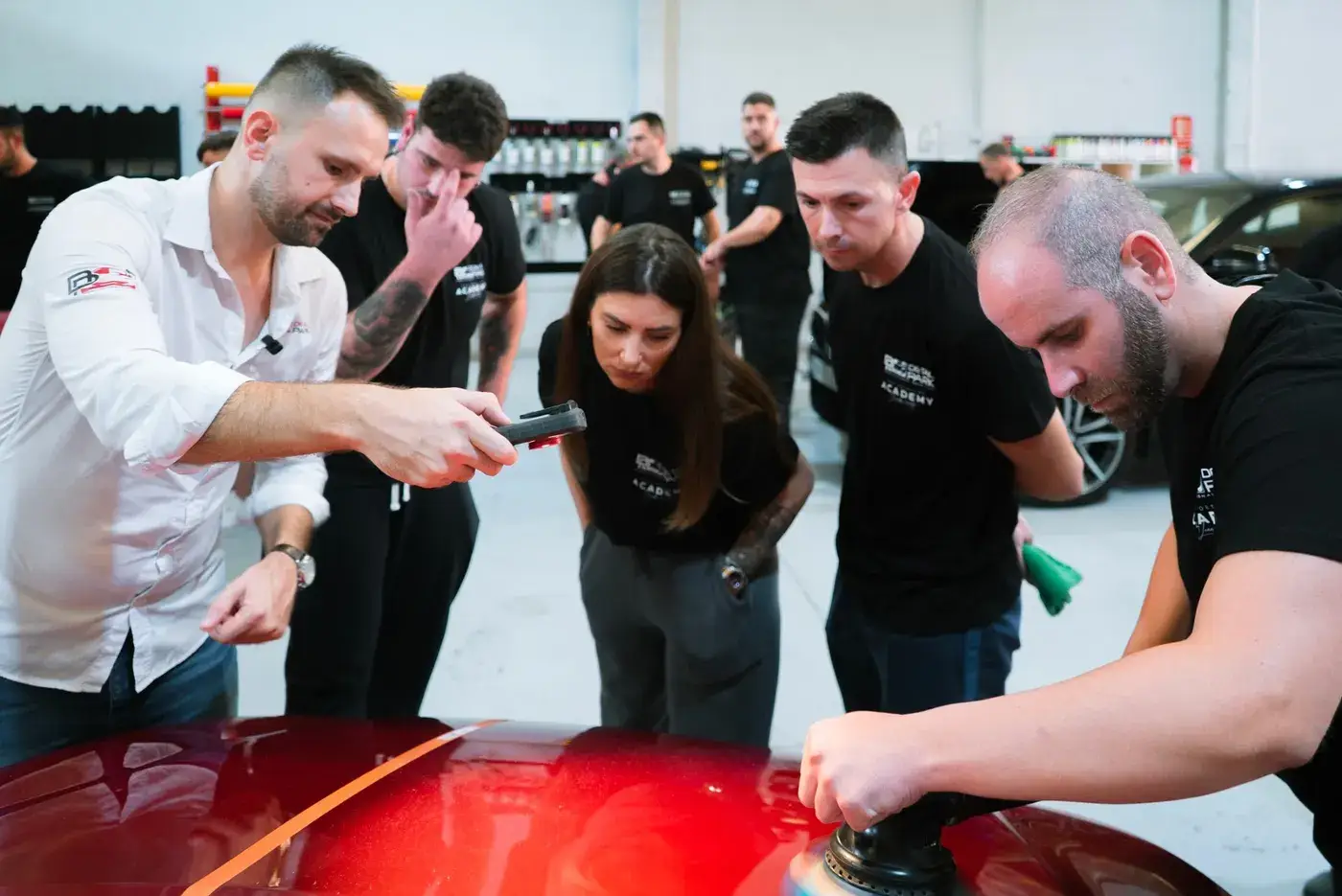 El instructor enseña a un grupo de alumnos a pulir un coche rojo