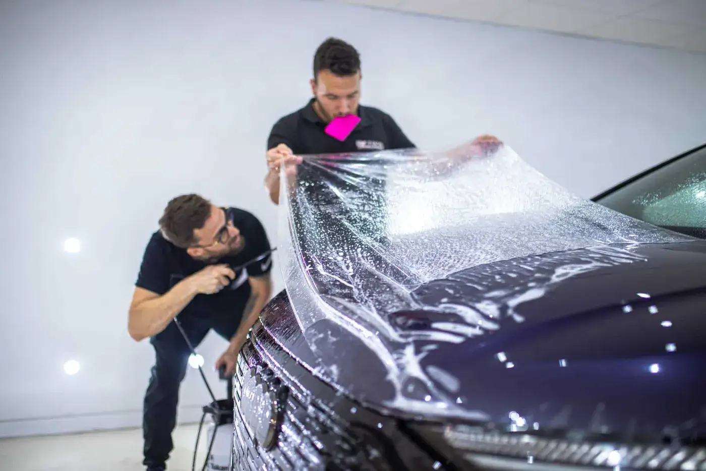 Dos instaladores de Detail Park colocando lámina PPF en el capó de un Audi